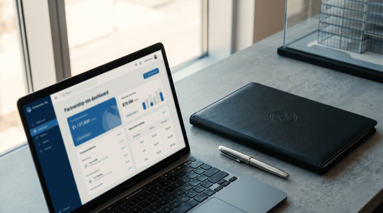 Laptop displaying a partnership tax dashboard beside a leather portfolio and pen on a modern office desk
